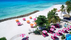 Un resort en la playa con arena blanca, agua turquesa y numerosos paraguas rosados y anaranjados que ofrecen sombra.