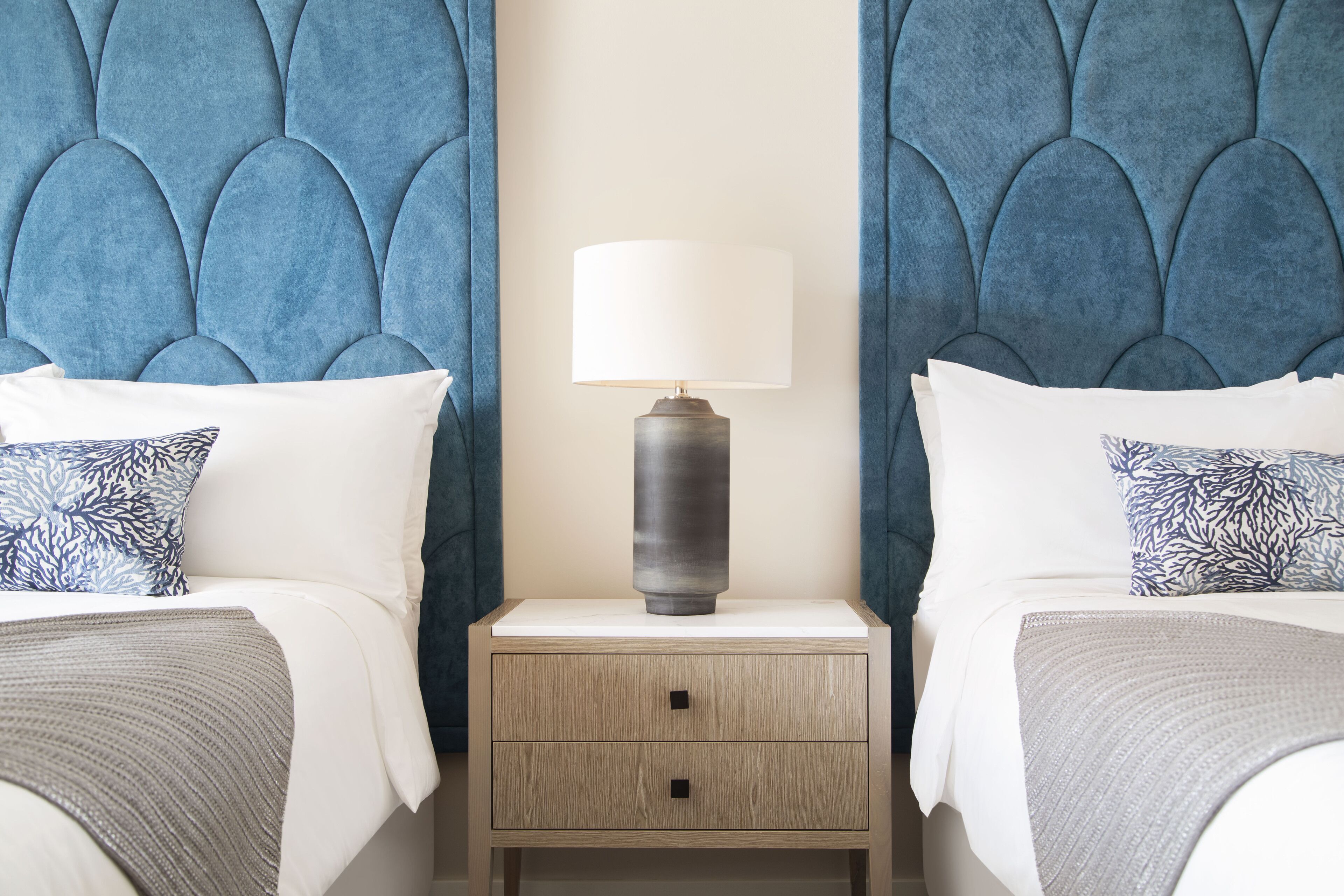 A bedroom with two beds, a nightstand with a lamp, and a headboard with a scalloped design.