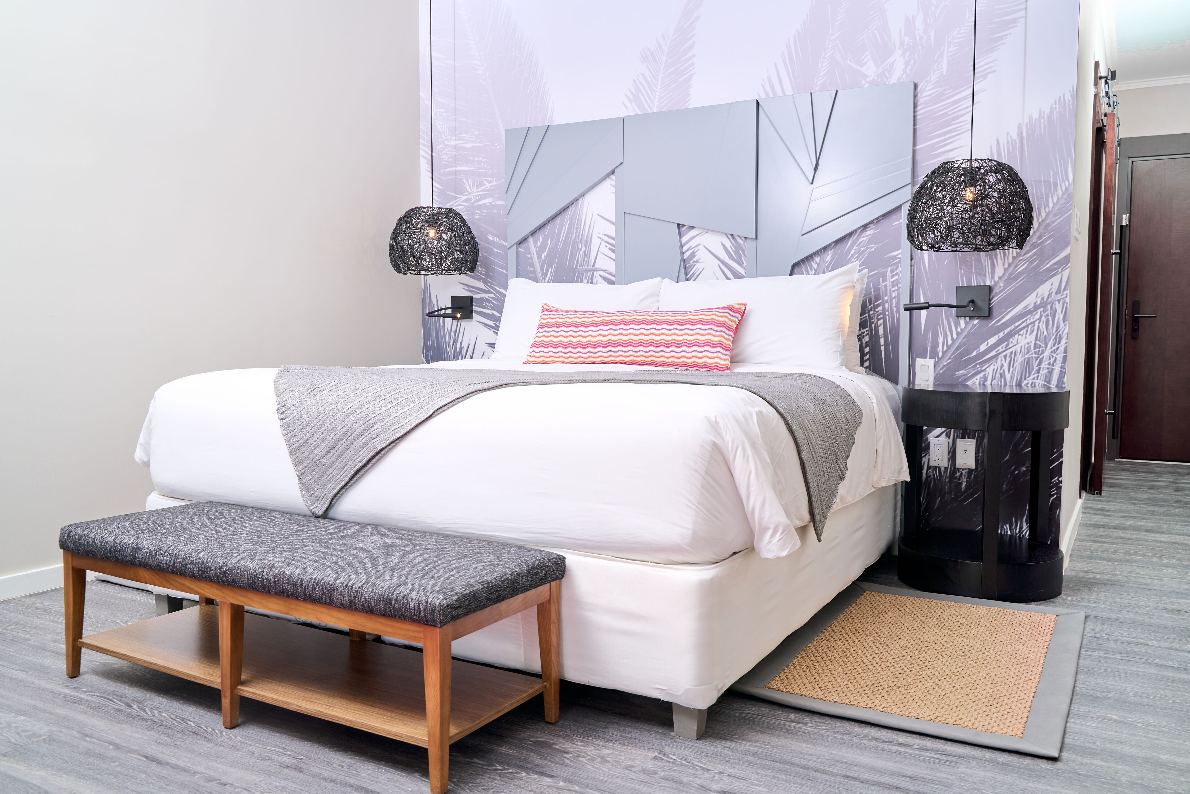 A modern bedroom with a bed, bench, nightstands, and a wall with abstract patterns.