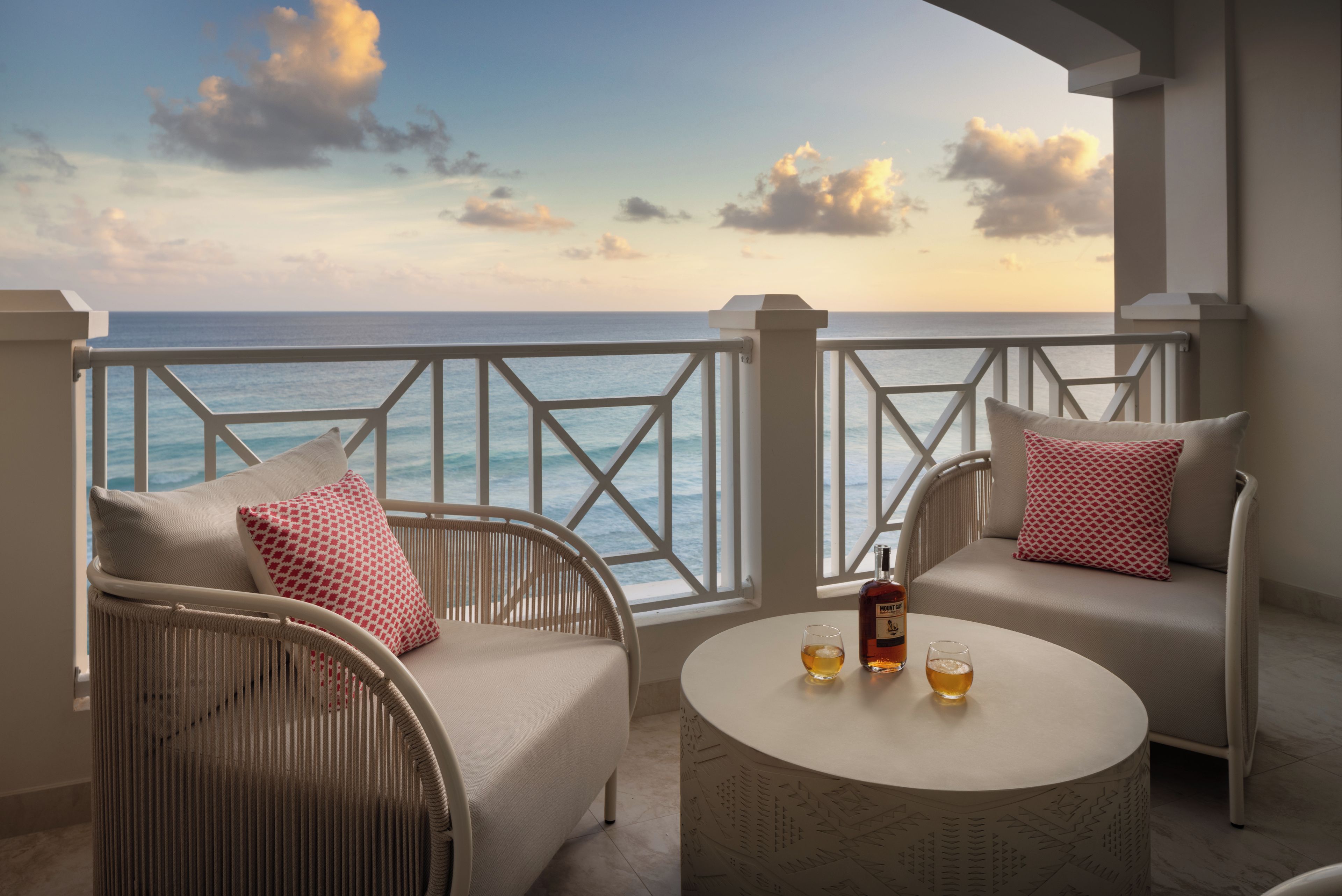 Een balkon met rieten meubels, een ronde tafel en een fles Mount Gay whiskey.