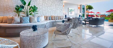 A modern lounge area with a seating arrangement, a patterned wall, and a view of the beach.