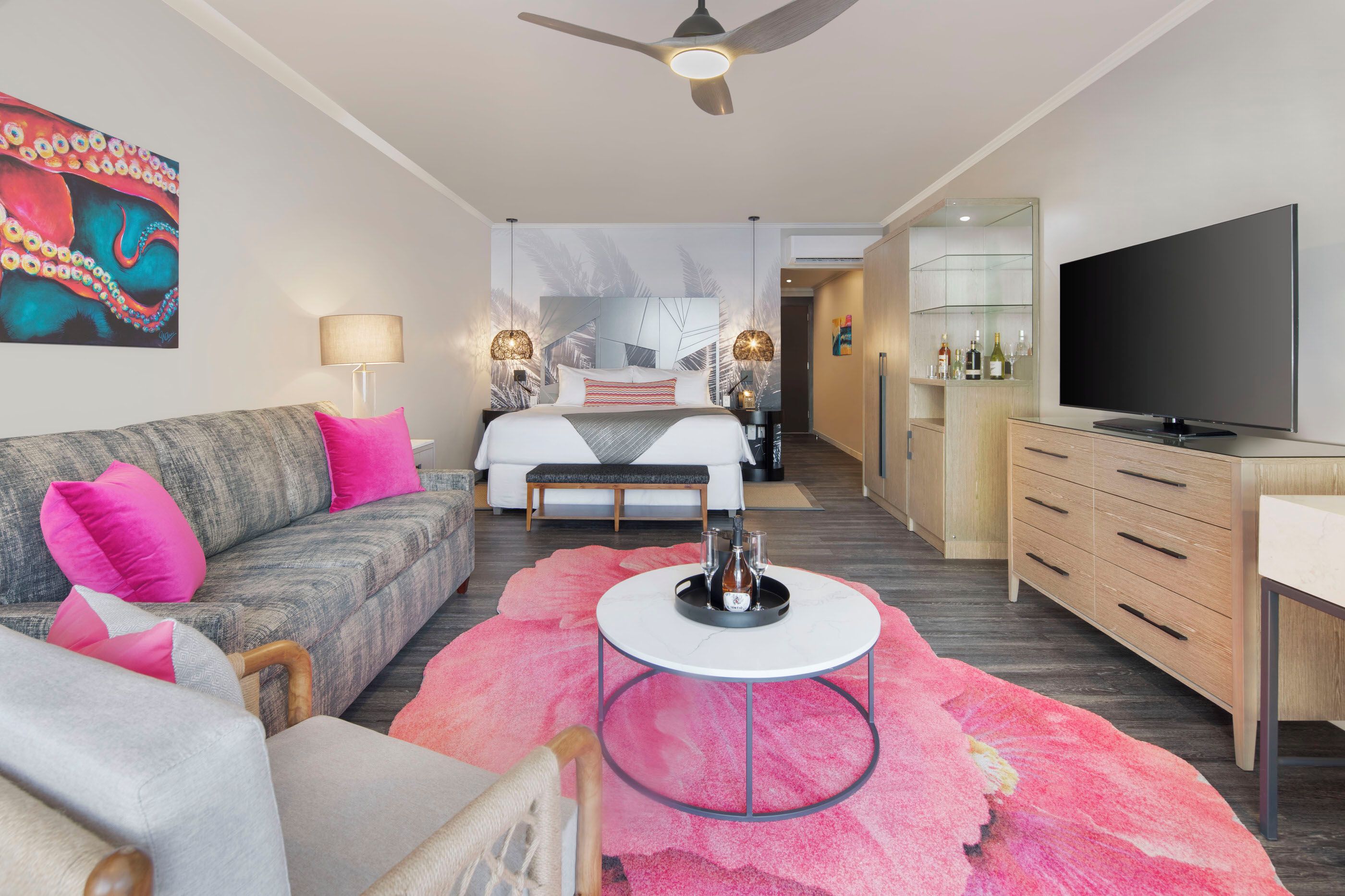 A modern hotel room with a bed, sofa, TV, and a dining area.