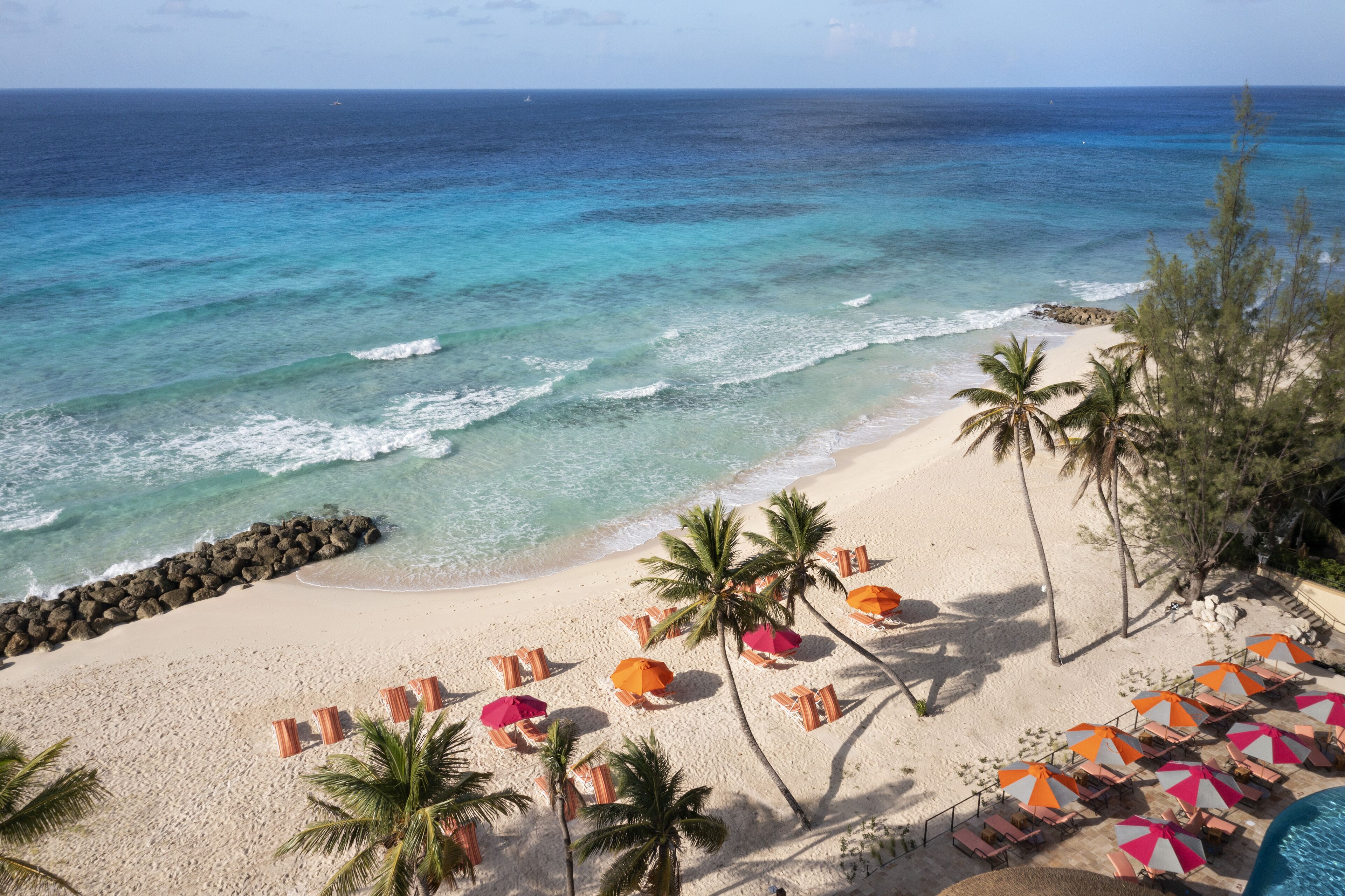 A beach with clear turquoise waters, a sandy shore, and rows of beach chairs and umbrellas.