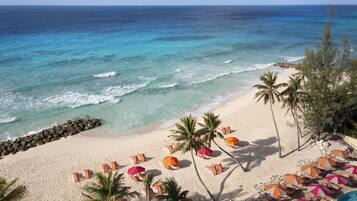 A beach with clear turquoise waters, a sandy shore, and rows of beach chairs and umbrellas.