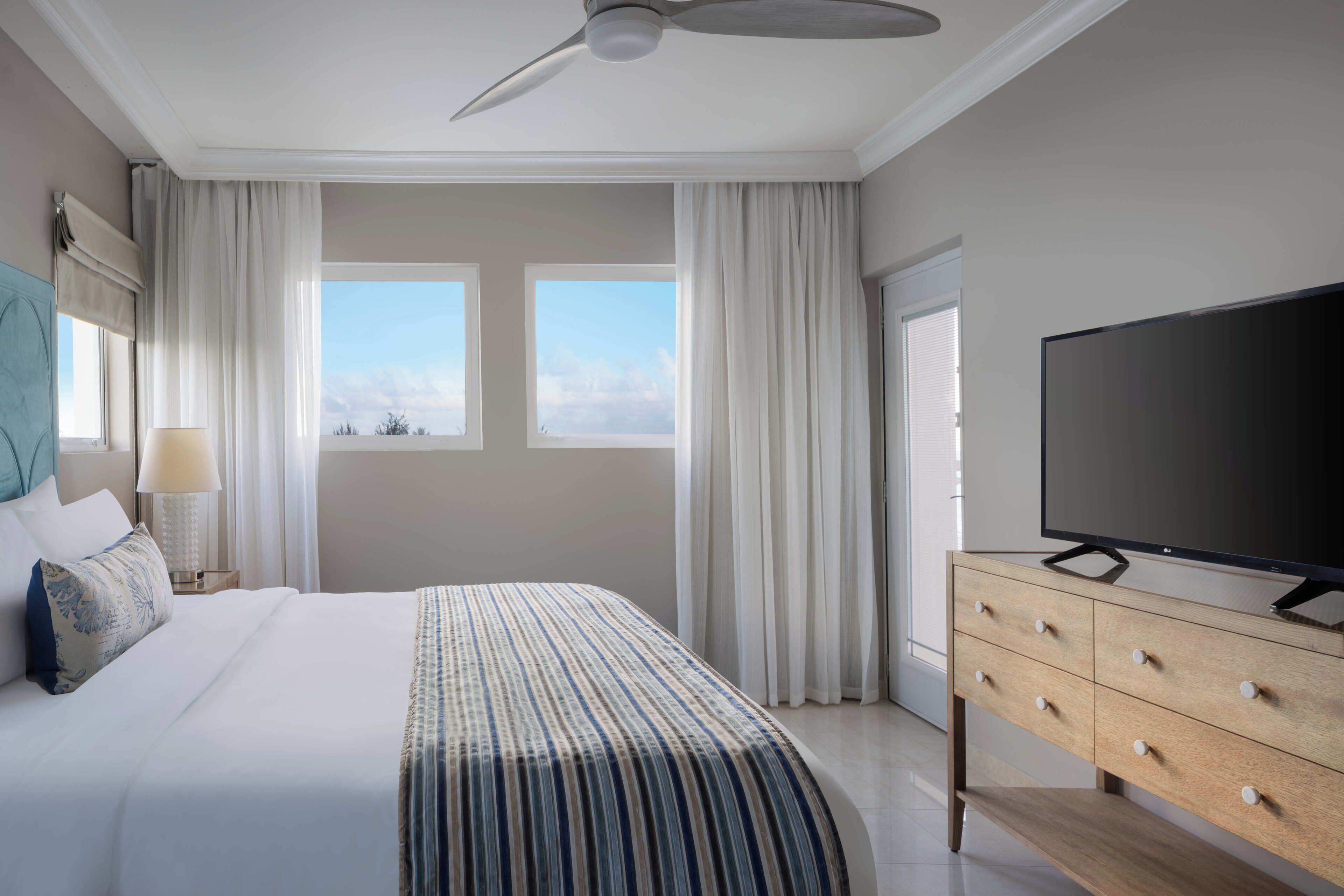 A hotel room with a large bed, a television, a wooden dresser, and a ceiling fan.