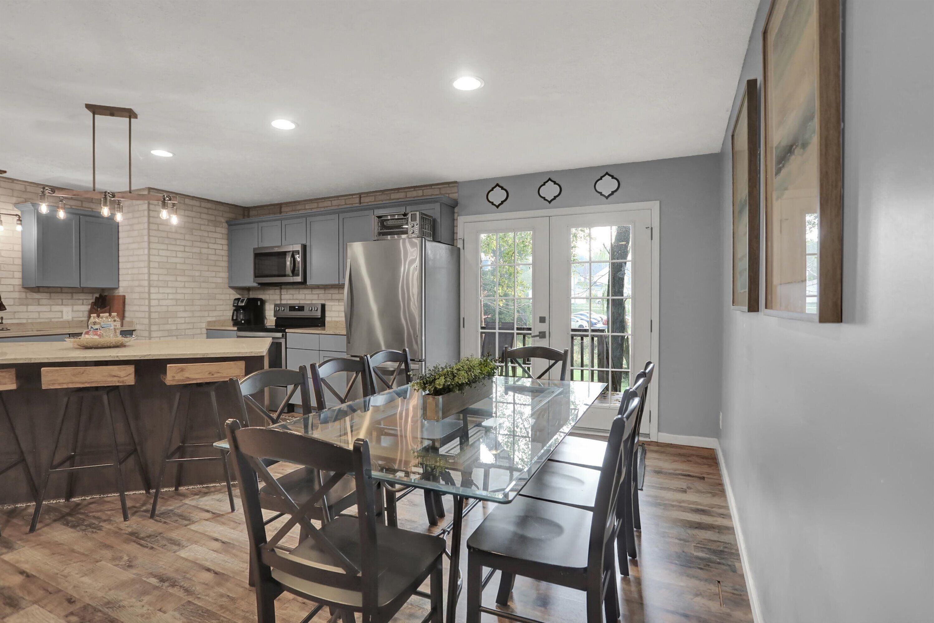 A modern kitchen with a central island, grey cabinets, and a large window.