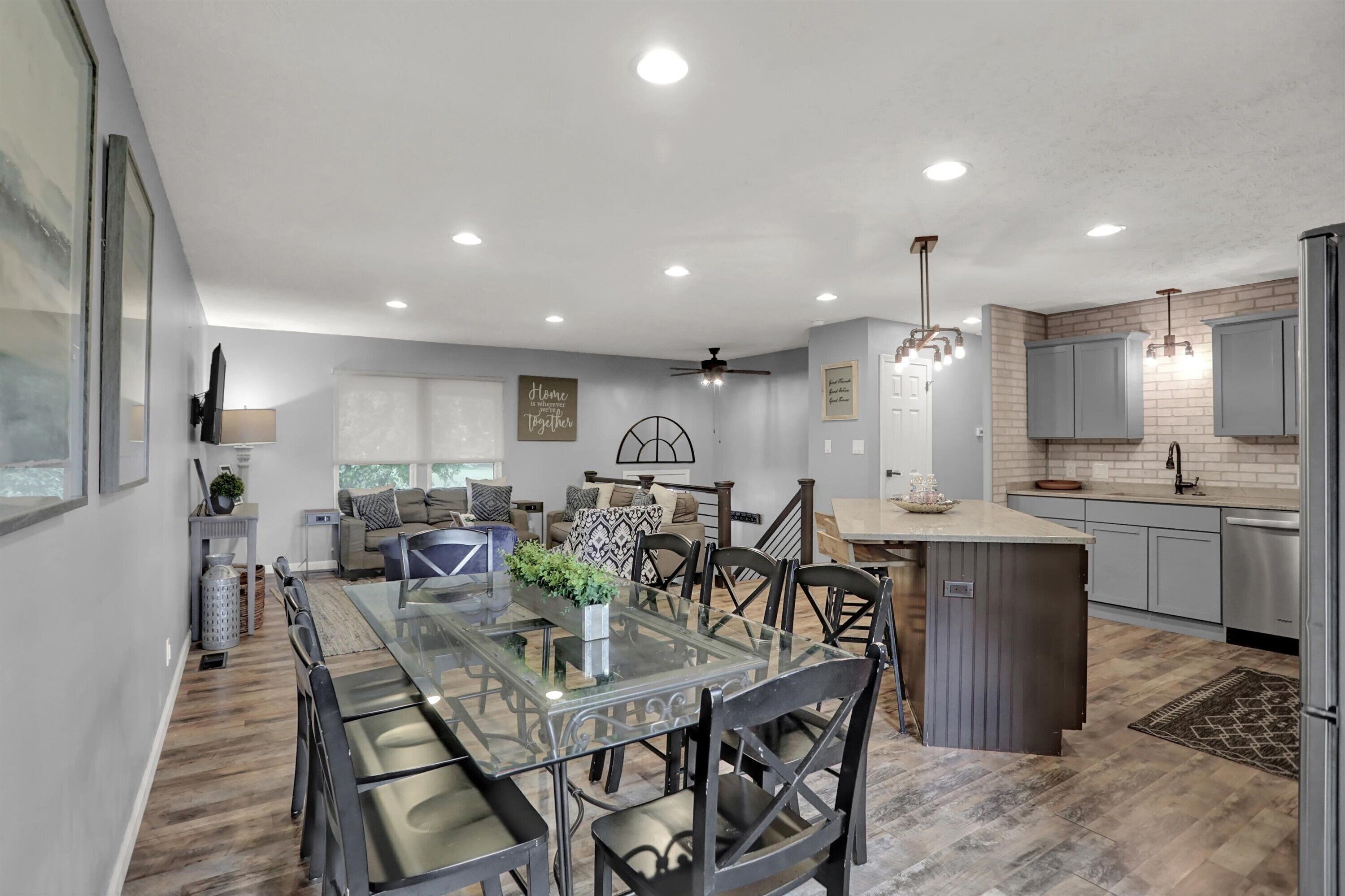 A modern kitchen with grey cabinets, a central island, and a dining area with a glass table and chairs.