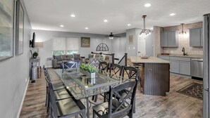 A modern kitchen with grey cabinets, a central island, and a dining area with a glass table and chairs.