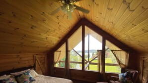 Una habitación tipo cabaña acogedora con una cama, una silla y un ventanal que ofrece vistas a un lago y follaje.
