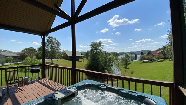 Un jacuzzi en una terraza de madera con vista a un lago y casas al fondo.