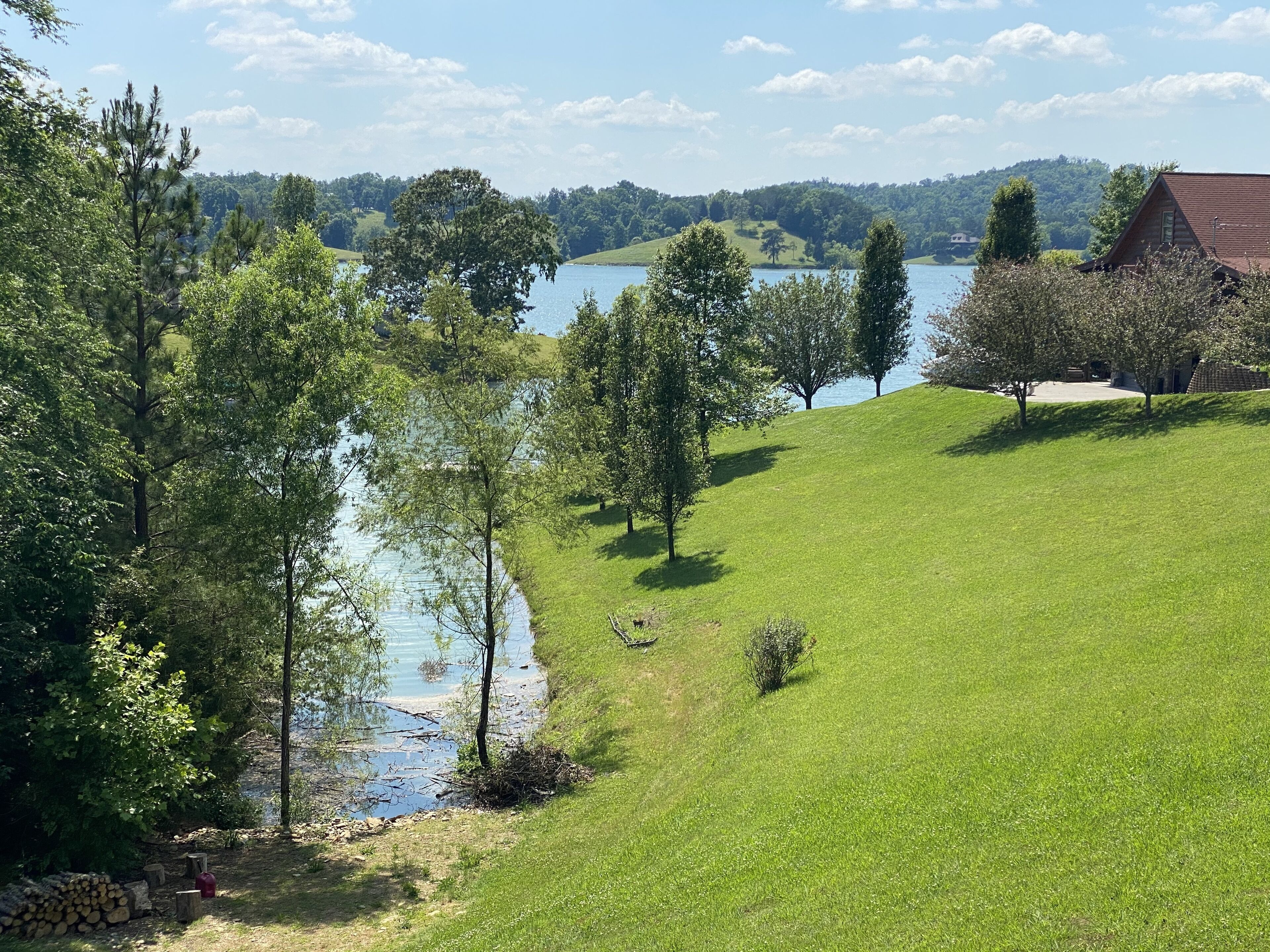A grassy hill with a lake, trees, and a building in the background.