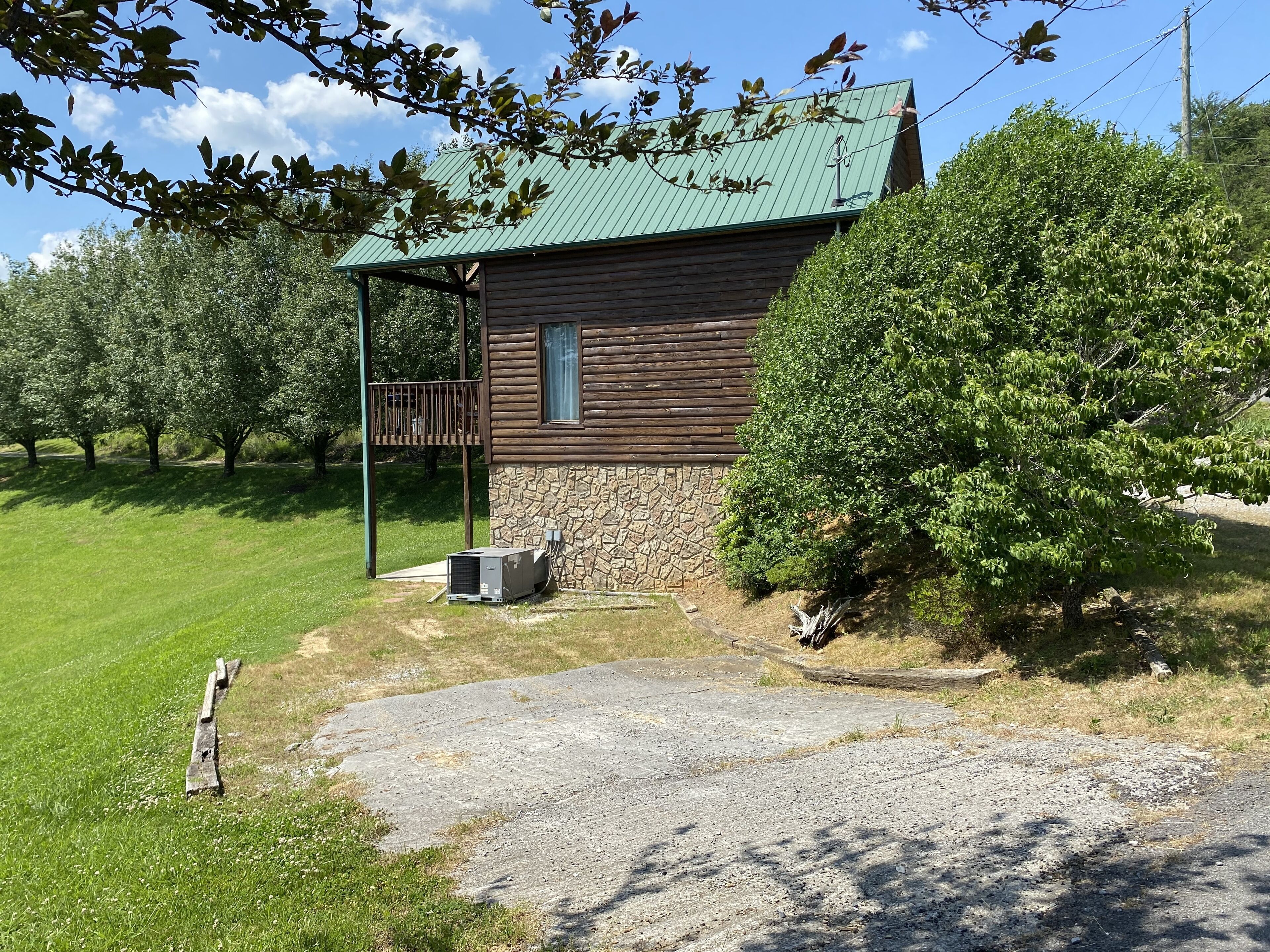 A rustic cabin with a stone foundation and wooden exterior, surrounded by lush greenery and a clear sky.