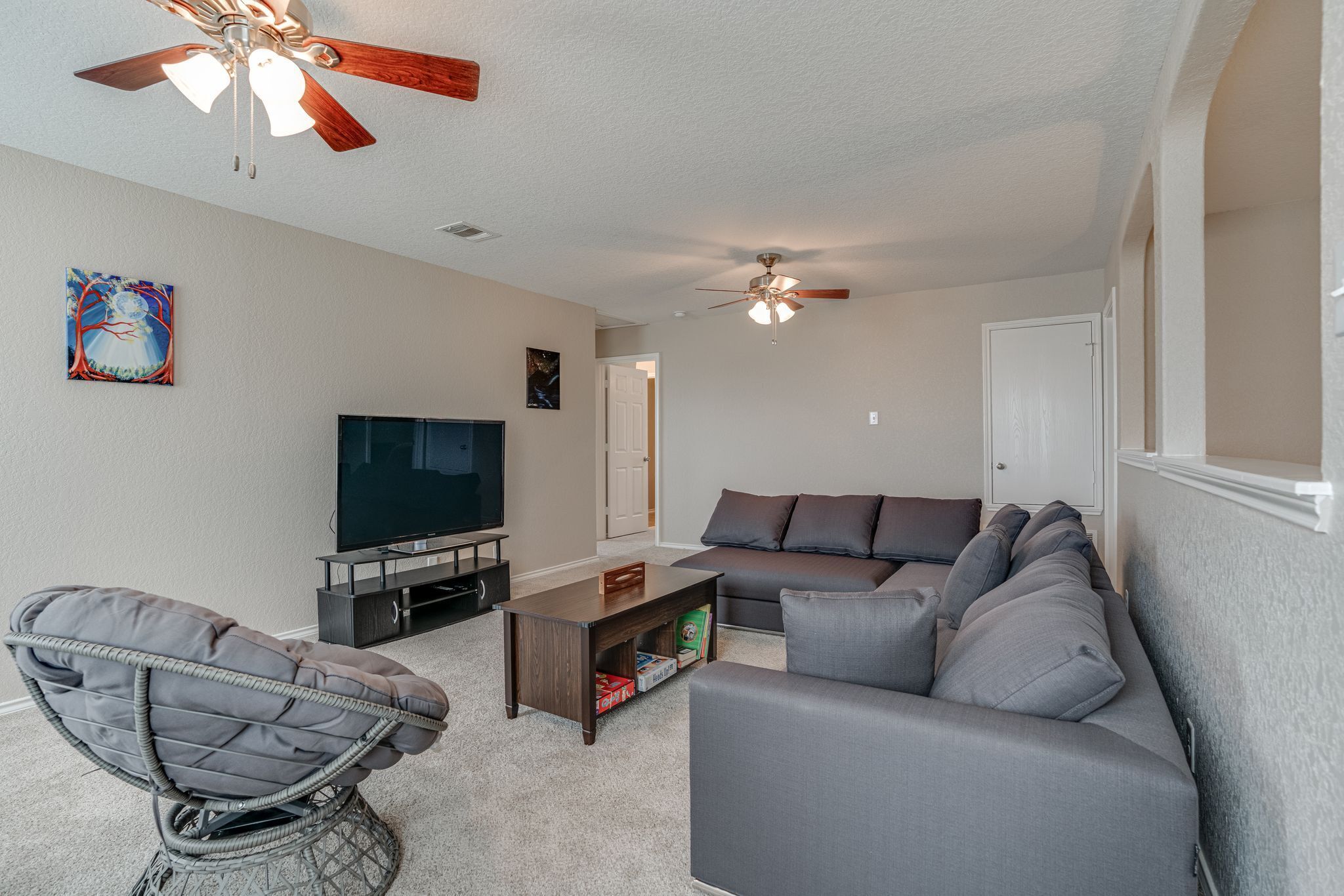 A living room with a gray sofa, a wicker chair, a coffee table, a TV, and two ceiling fans.