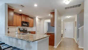 A kitchen with granite countertops, wooden cabinets, and a central island with seating. - Corporate, Lackland, Sea World, Alamo, Fiesta, Riverwalk BMT graduation (San Antonio)