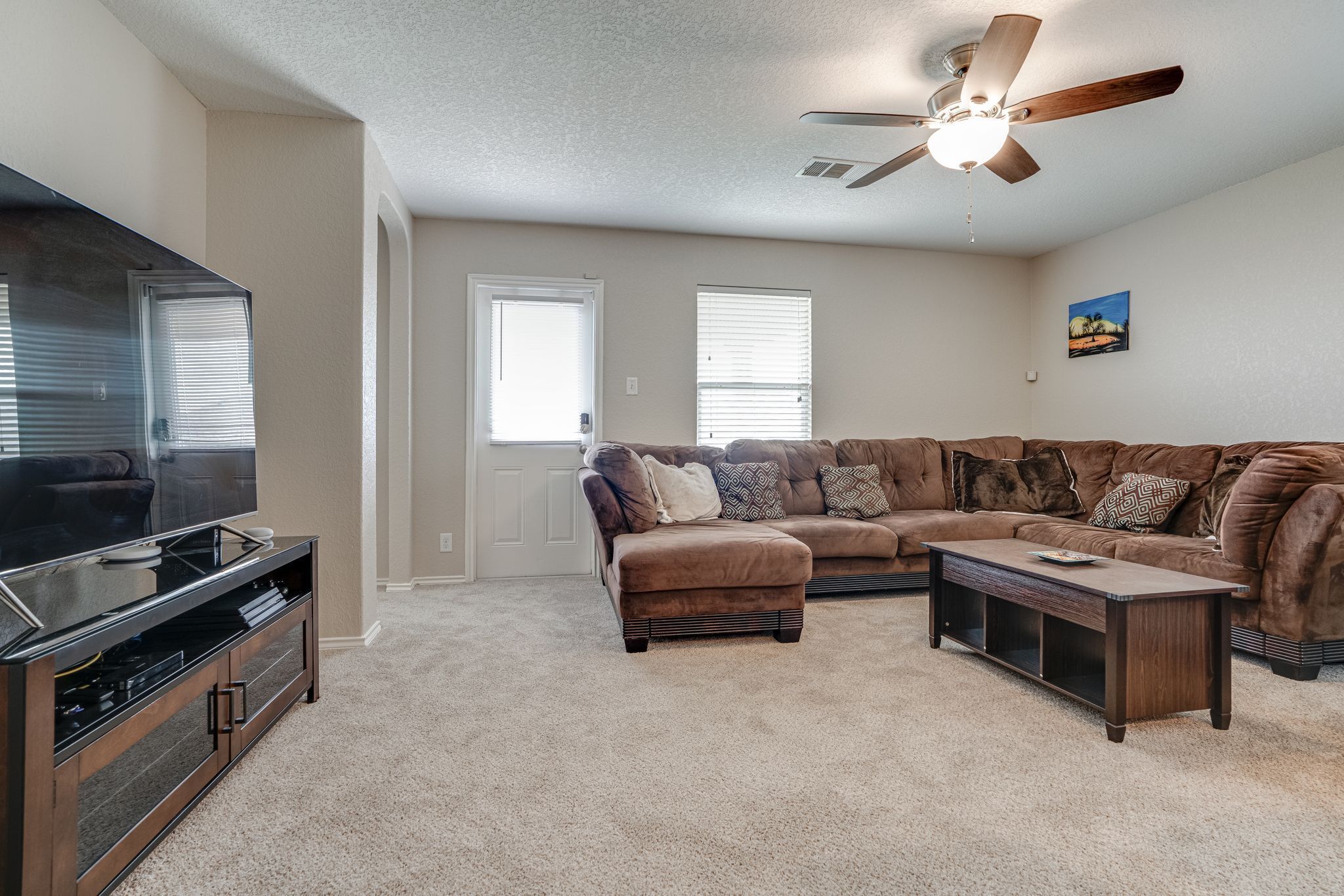A living room with a sectional sofa, a flat-screen TV, a wooden coffee table, and a ceiling fan.