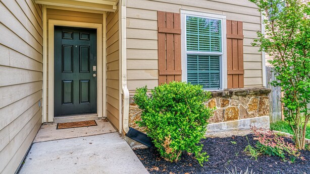A house with a dark front door, a window with shutters, and a small garden area with mulch and plants. - Corporate, Lackland, Sea World, Alamo, Fiesta, Riverwalk BMT graduation (San Antonio)