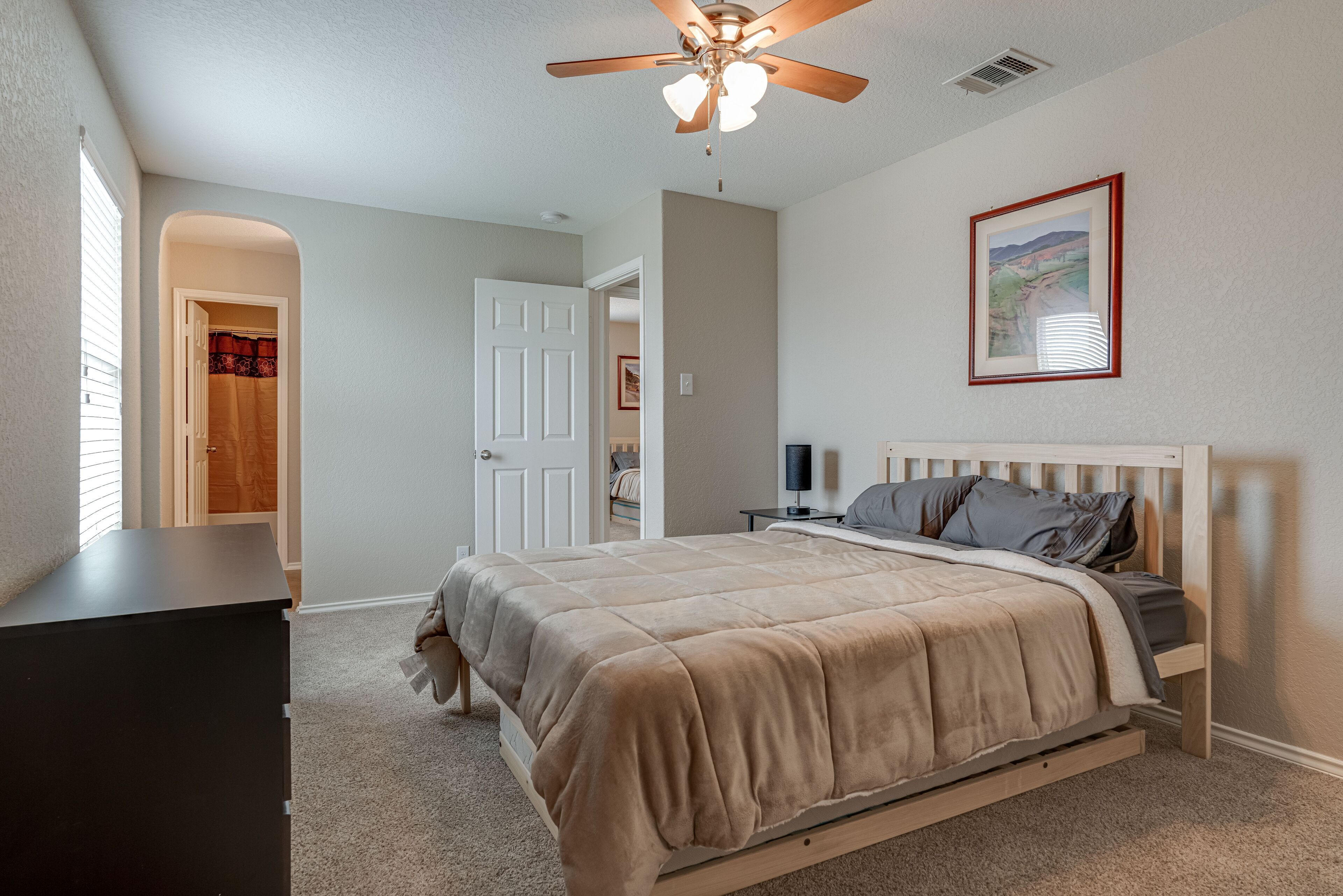 A bedroom with a bed, a ceiling fan, a TV, and a door leading to another room.