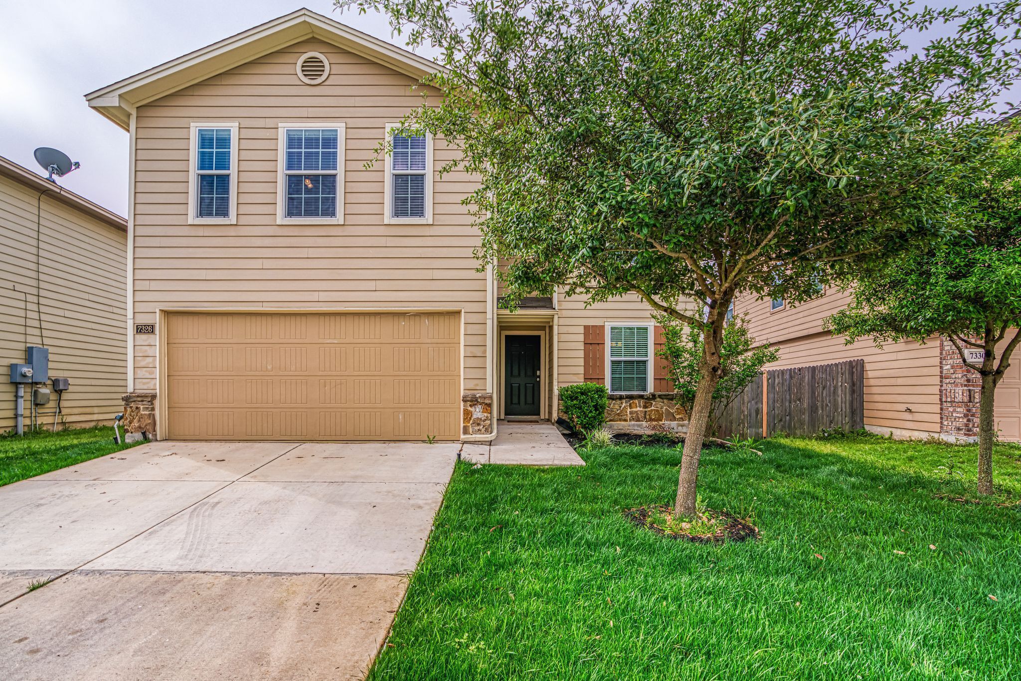 A two-story house with a garage, a tree in the front yard, and a satellite dish on the roof.