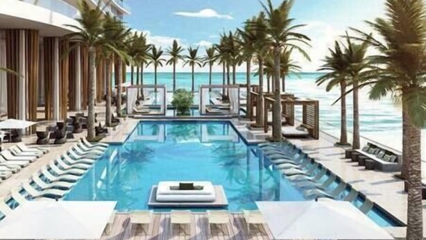 A pool area with lounge chairs and palm trees, overlooking the ocean.