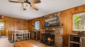 A cozy room with a stone fireplace, wooden furniture, and a ceiling fan. - Bear Slope View - Close to Slopes, Pet Friendly, Fenced Yard, Hot Tub (Big Bear Lake)