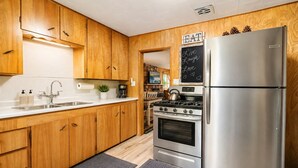 A kitchen with wooden cabinets, stainless steel appliances, a chalkboard with 'EAT Live Laugh Love' message, and a stone wall in the background. - Bear Slope View - Close to Slopes, Pet Friendly, Fenced Yard, Hot Tub (Big Bear Lake)