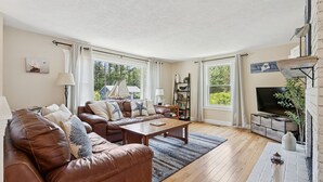 Een ruime woonkamer met een bruine leren bank, een houten salontafel en een televisie op een houten dressoir.