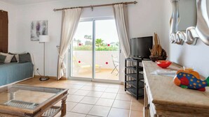 A living room with a sofa, a coffee table, a TV, a balcony with a view, and a decorative mirror. - Villa White Sands - Private Oasis, Heated Pool, Beaches & Strip Nearby (Albufeira)