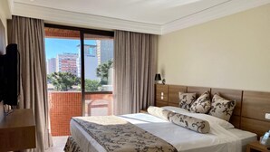 A hotel room with a large bed, a desk, and a view of the city through the balcony. - Hotel Wynn Batel (Curitiba)