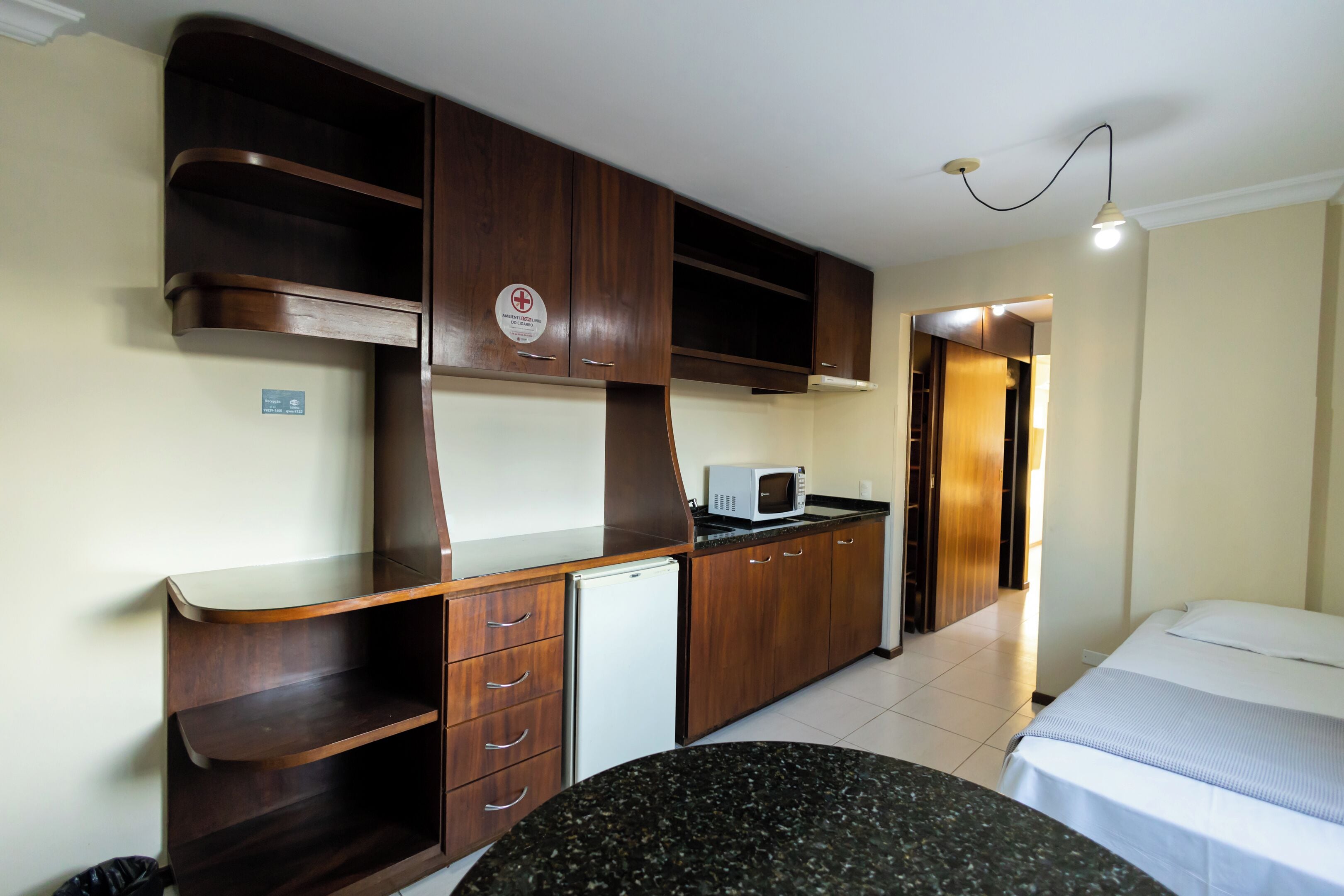 Een kleine kamer met een kitchenette, een bed en een klein rond tafeltje.