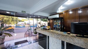 A hotel reception area with a marble counter, a television, and a view of the street outside. - Hotel Wynn Batel (Curitiba)