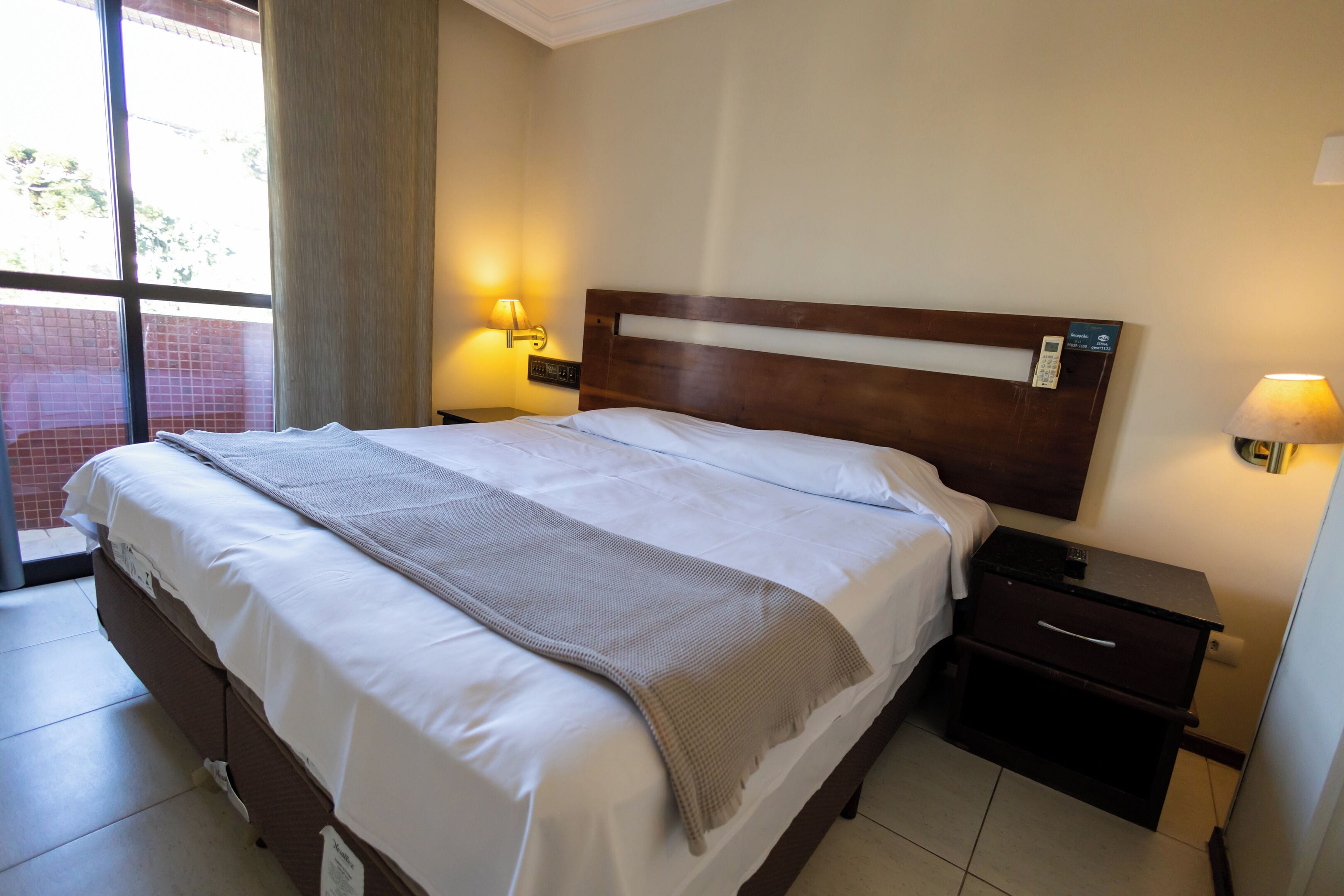 Una camera d'albergo con un letto grande, due comodini con lampade, una finestra con tende e vista sull'esterno.