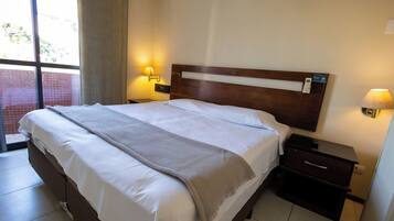 Una camera d'albergo con un letto grande, due comodini con lampade, una finestra con tende e vista sull'esterno.