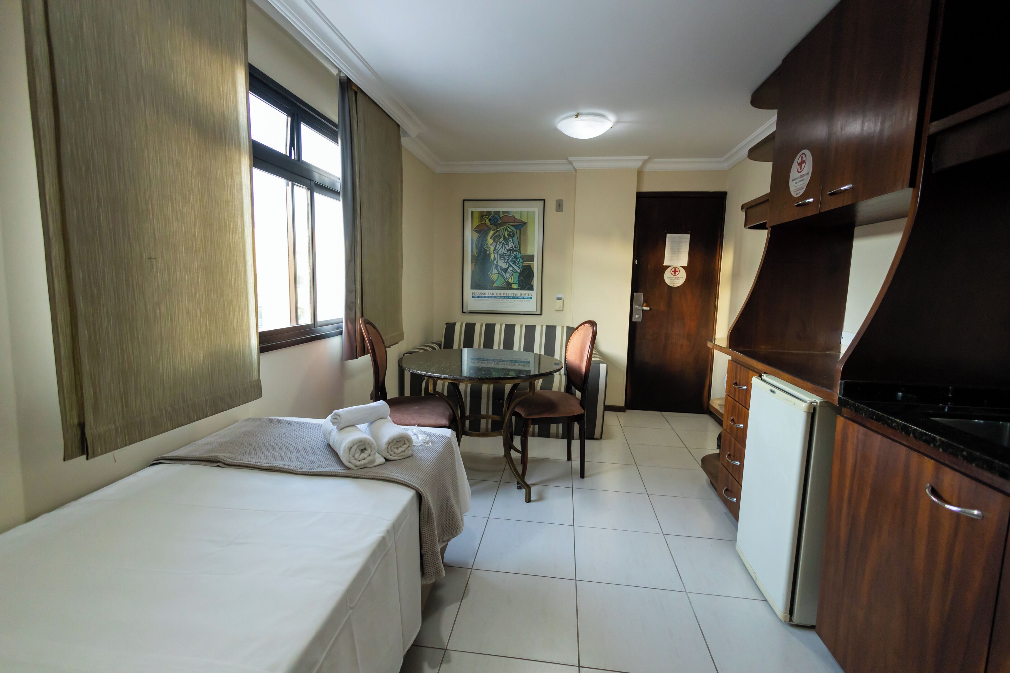 Una habitación de hotel compacta con cama, una pequeña mesa de comedor, sillas, refrigerador y kitchenette.