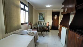 Una habitación de hotel compacta con cama, una pequeña mesa de comedor, sillas, refrigerador y kitchenette.