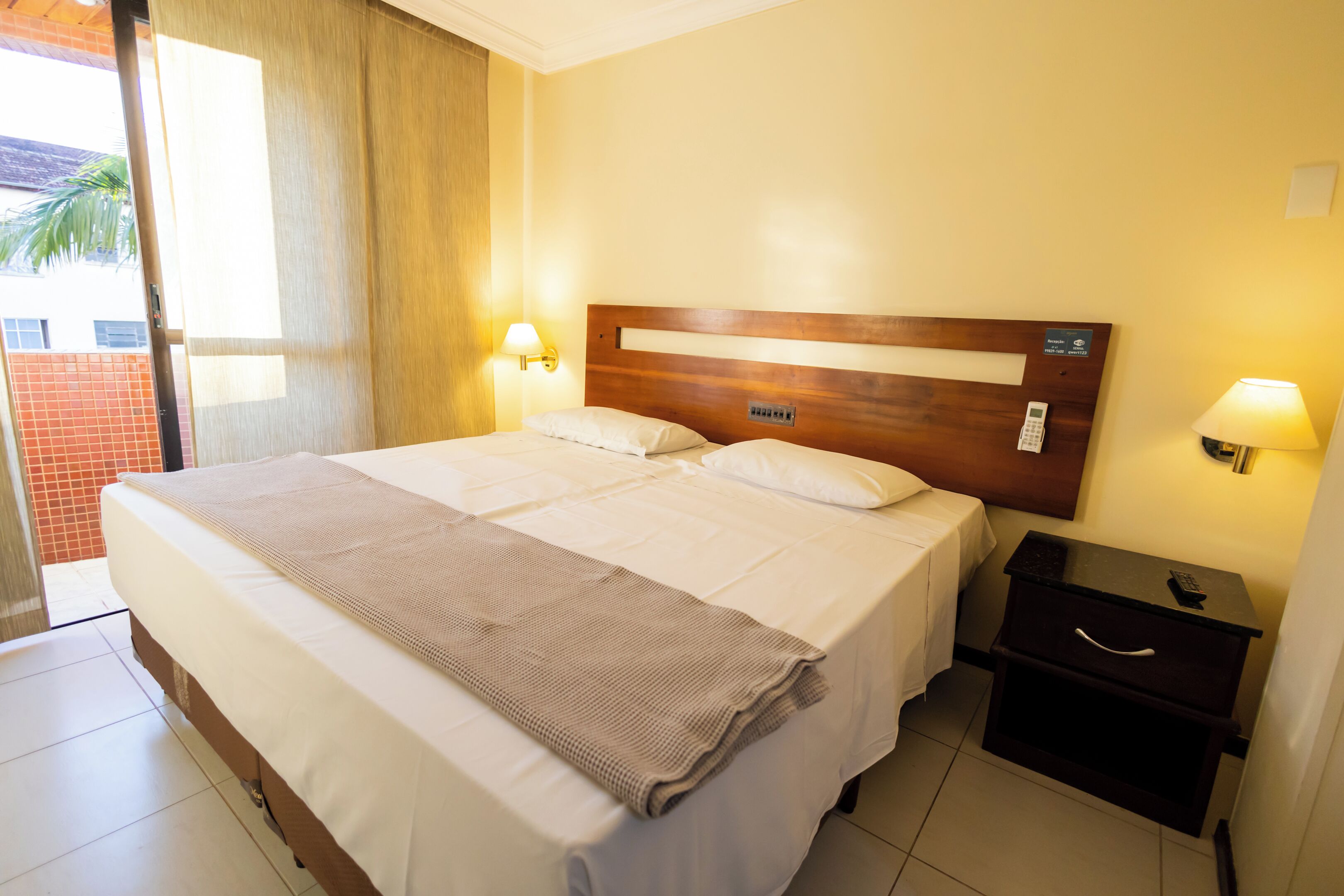 A hotel room with a large bed, two bedside tables, a nightstand, and a view of the outside.