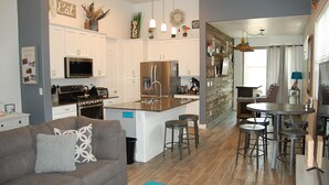A modern kitchen with white cabinets, a central island with stools, and a dining area with a round table and chairs. - Beautiful New Townhome nestled in the Pines! (Flagstaff)