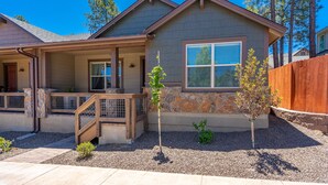 A residential house with a covered porch, stone accents, and a wooden fence. - Beautiful New Townhome nestled in the Pines! (Flagstaff)