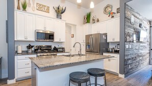 A modern kitchen with white cabinets, granite countertops, stainless steel appliances, and a central island with bar stools. - Beautiful New Townhome nestled in the Pines! (Flagstaff)