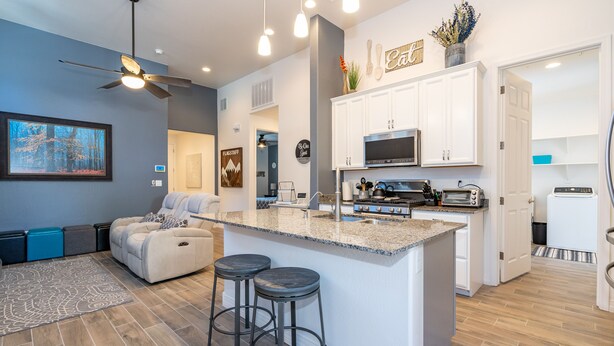 A modern kitchen with white cabinets, a granite countertop, and a built-in oven. There are two bar stools and a ceiling fan. - Beautiful New Townhome nestled in the Pines! (Flagstaff)