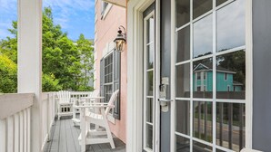 A covered porch with white chairs and tables, a door with a keypad lock, and a view of a turquoise house in the background. - 41 Bradley, Private Pool, Newly Updated, Close to Beach, Free Golf (Hilton Head Island)