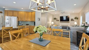 A modern kitchen with wooden cabinets, a dining table with chairs, a chandelier, and a living area with a sofa and TV. - 41 Bradley, Private Pool, Newly Updated, Close to Beach, Free Golf (Hilton Head Island)