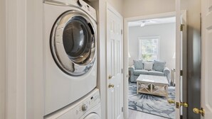 A laundry room with a front-loading washing machine, a door leading to a living area with a sofa and a coffee table. - 41 Bradley, Private Pool, Newly Updated, Close to Beach, Free Golf (Hilton Head Island)
