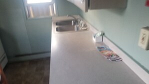 Una cocina con encimera blanca, un lavamanos y una ventana con persianas.