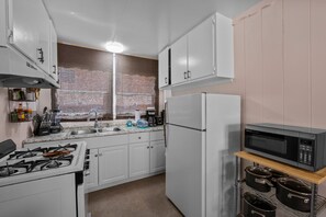 Une cuisine avec des meubles blancs, un évier en acier inoxydable, une cuisinière à gaz, un réfrigérateur et un four à micro-ondes.