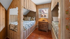 Ein schlicht eingerichtetes Schlafzimmer im Blockhausstil mit schrägem Dach, Holzwänden und einem Fenster mit Aussicht.