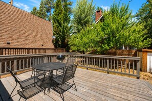 A wooden deck with a round table and chairs, surrounded by a wooden fence, and trees in the background.