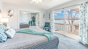 Een slaapkamer met een groot bed, een plafondventilator en een glazen schuifdeur naar een balkon met uitzicht op het water.