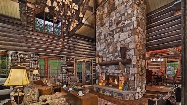 L’intérieur d’une cabane en rondins, avec une cheminée en pierre, des meubles en bois et un lustre.