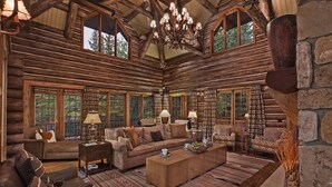 L’intérieur d’une cabane en rondins, avec un grand canapé, deux fauteuils, une table basse et un lustre.