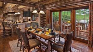 Un intérieur de style rustique, aménagé comme un chalet, avec un coin repas, une cuisine et de grandes fenêtres donnant sur un jardin.